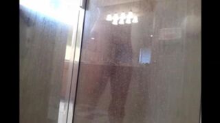 A guy washes his body in the shower, unaware of being watched
