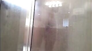 A guy washes his body in the shower, unaware of being watched