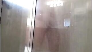 A guy washes his body in the shower, unaware of being watched