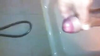 The kid masturbates his dick under the jet of water in the shower